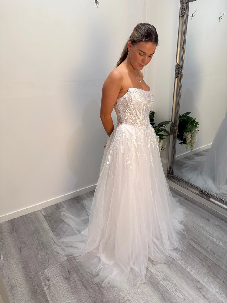 Young woman wearing a white debutante dress with lace bodice and tulle skirt, standing in a bridal fitting room at Divine Bridal.