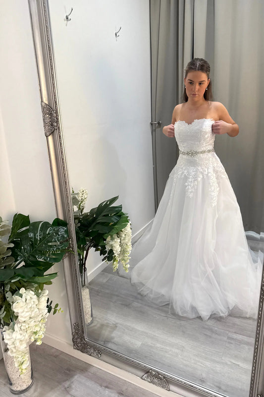 Model looking in mirror wearing Libby Debutante Dress with lace bodice – front view.