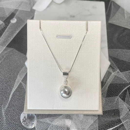 Introducing the Merlin Silver Necklace, a round silver pendant necklace with intricate design details. The pendant is complemented by a round ball. Suitable for casual and formal attire.
