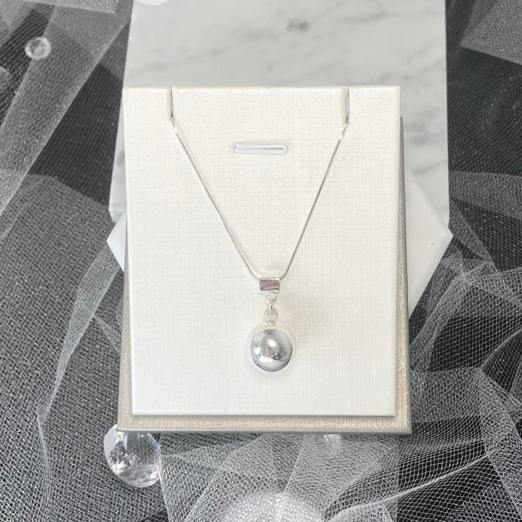 Introducing the Merlin Silver Necklace, a round silver pendant necklace with intricate design details. The pendant is complemented by a round ball. Suitable for casual and formal attire.