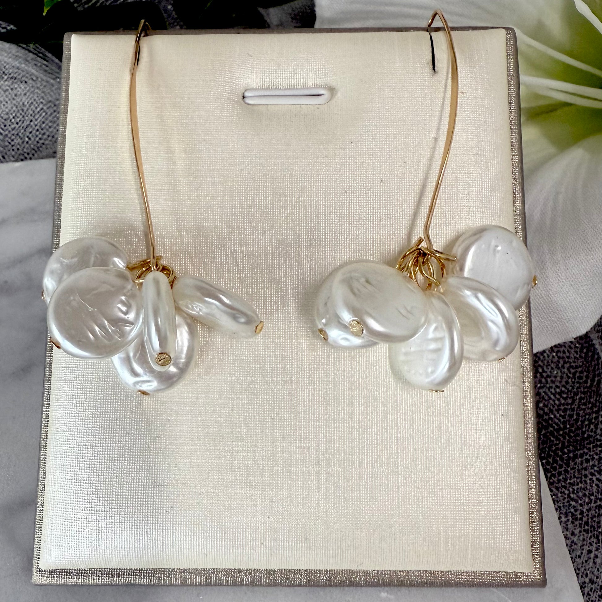 Pair of gold earrings with flat round-shaped pearls on a beige display card.