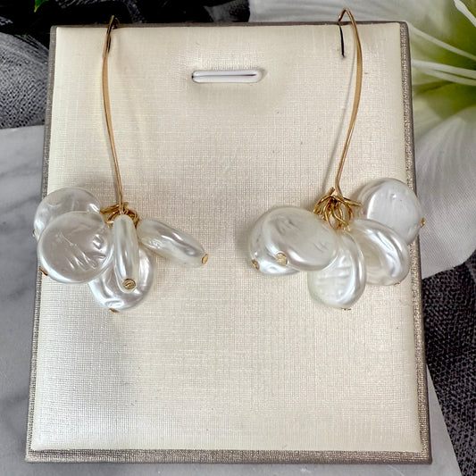 Pair of gold earrings with flat round-shaped pearls on a beige display card.