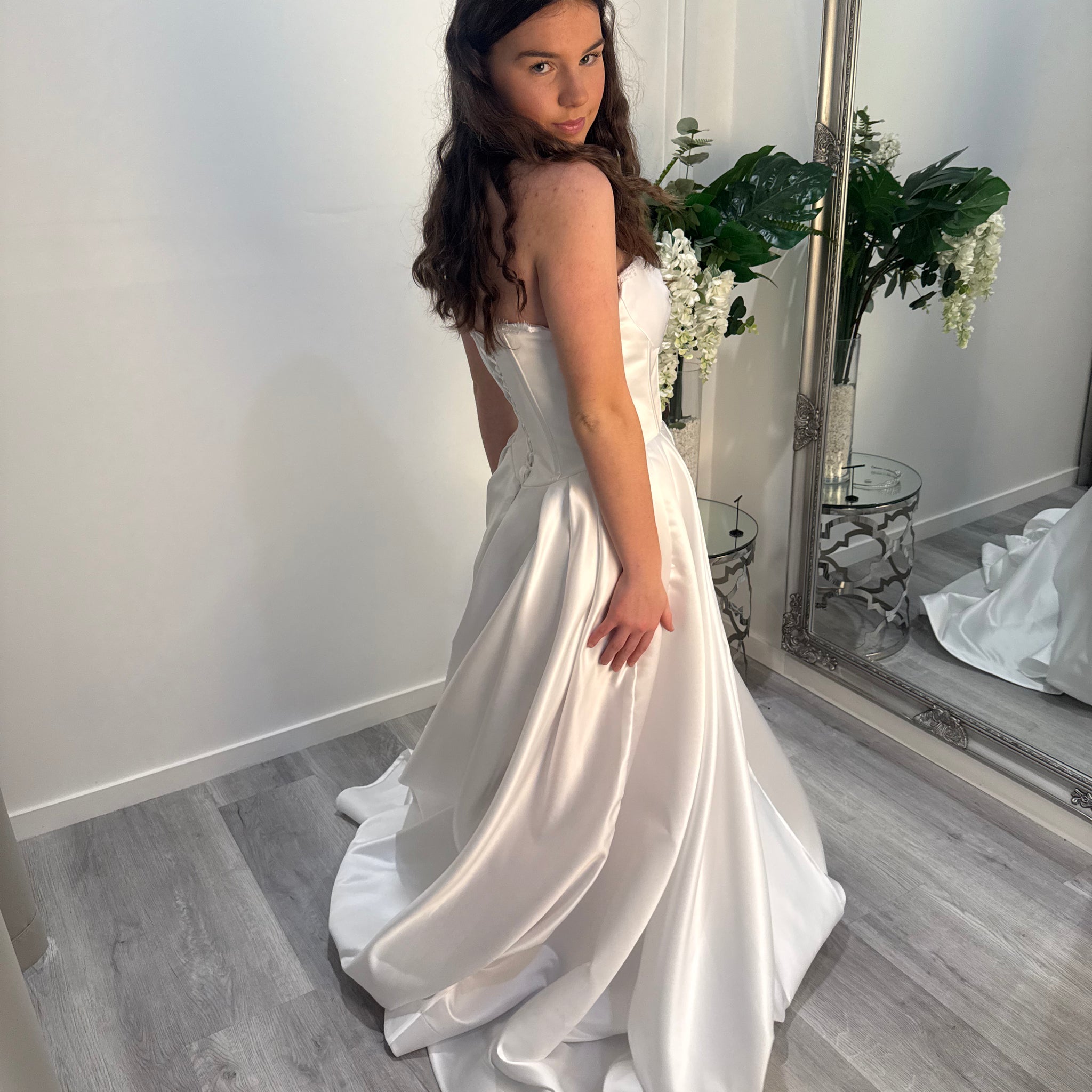 Woman in a white deb dress standing in a room with a mirror and flowers.