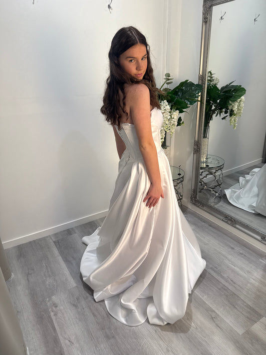 Woman in a white deb dress standing in a room with a mirror and flowers.