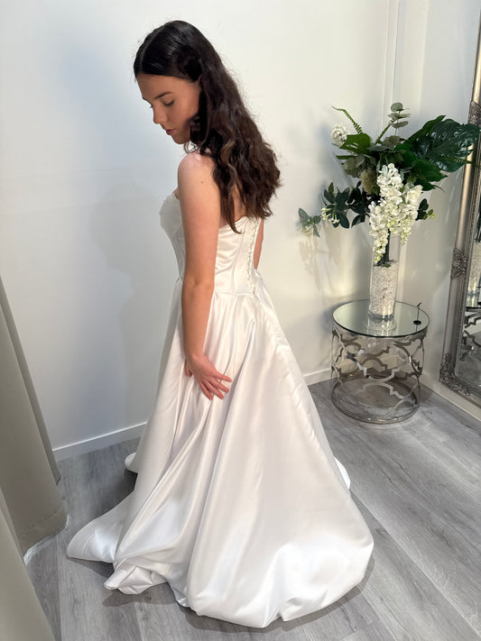 Woman in a white debutante dress standing in a room with a vase of flowers on a table.