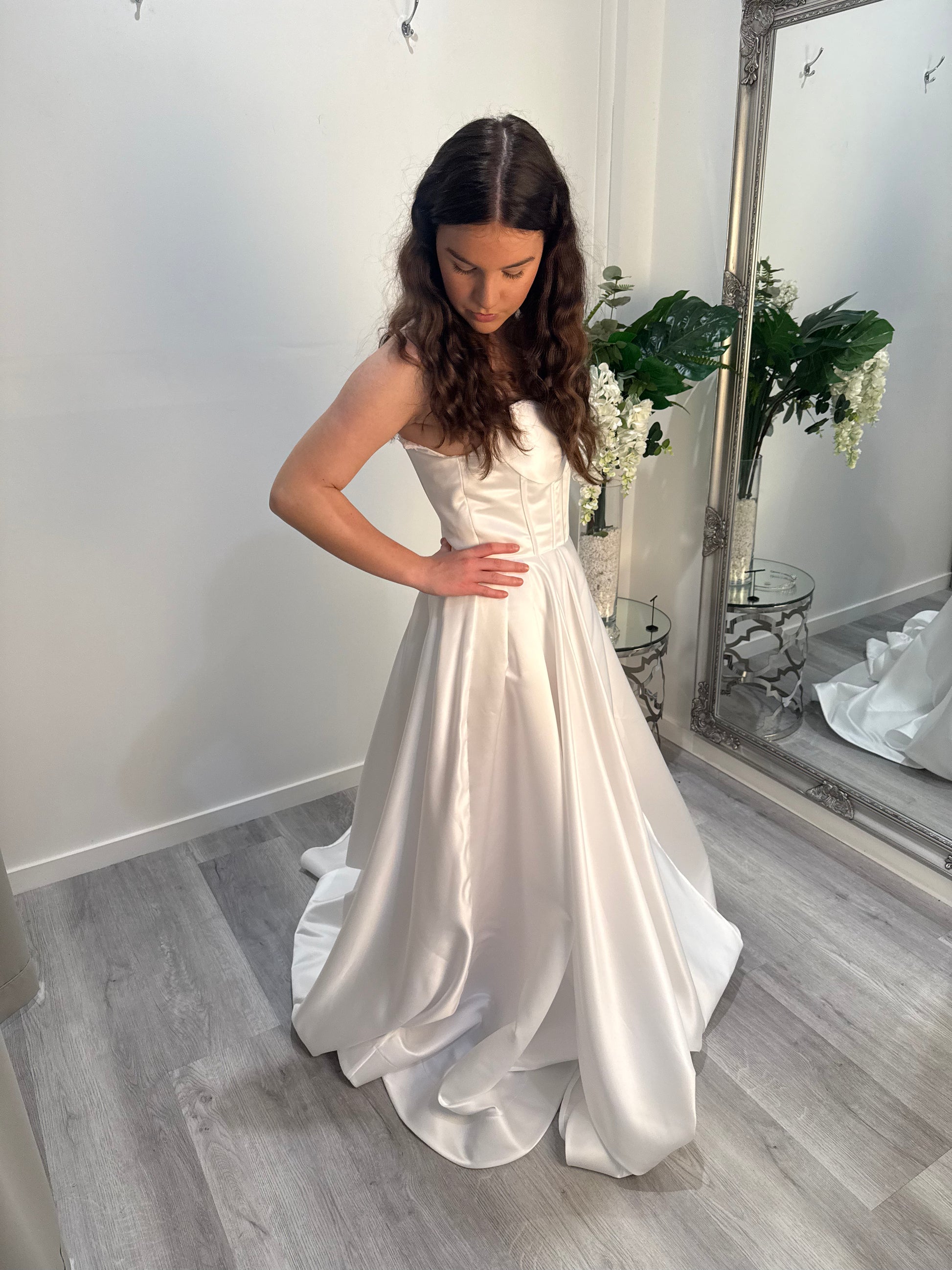 Woman in a white strapless gown standing in a room with a mirror and decor.