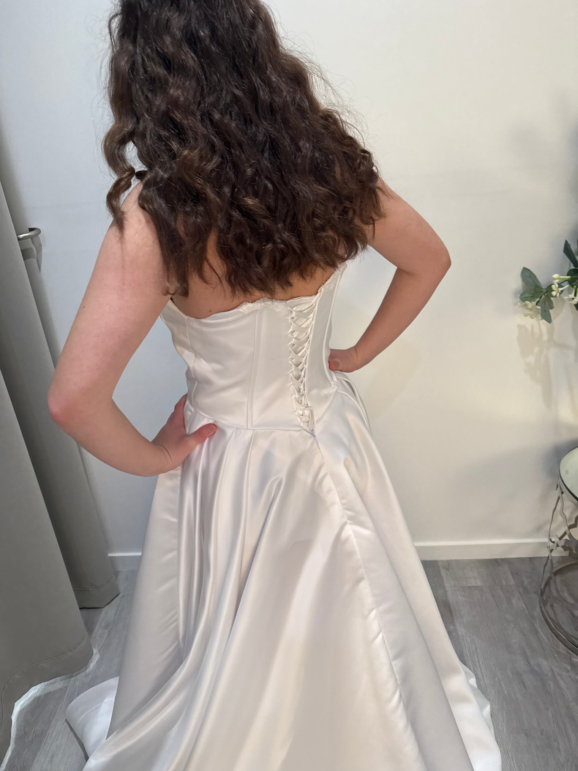 Person wearing a white strapless dress with a corset-style bodice in a room.