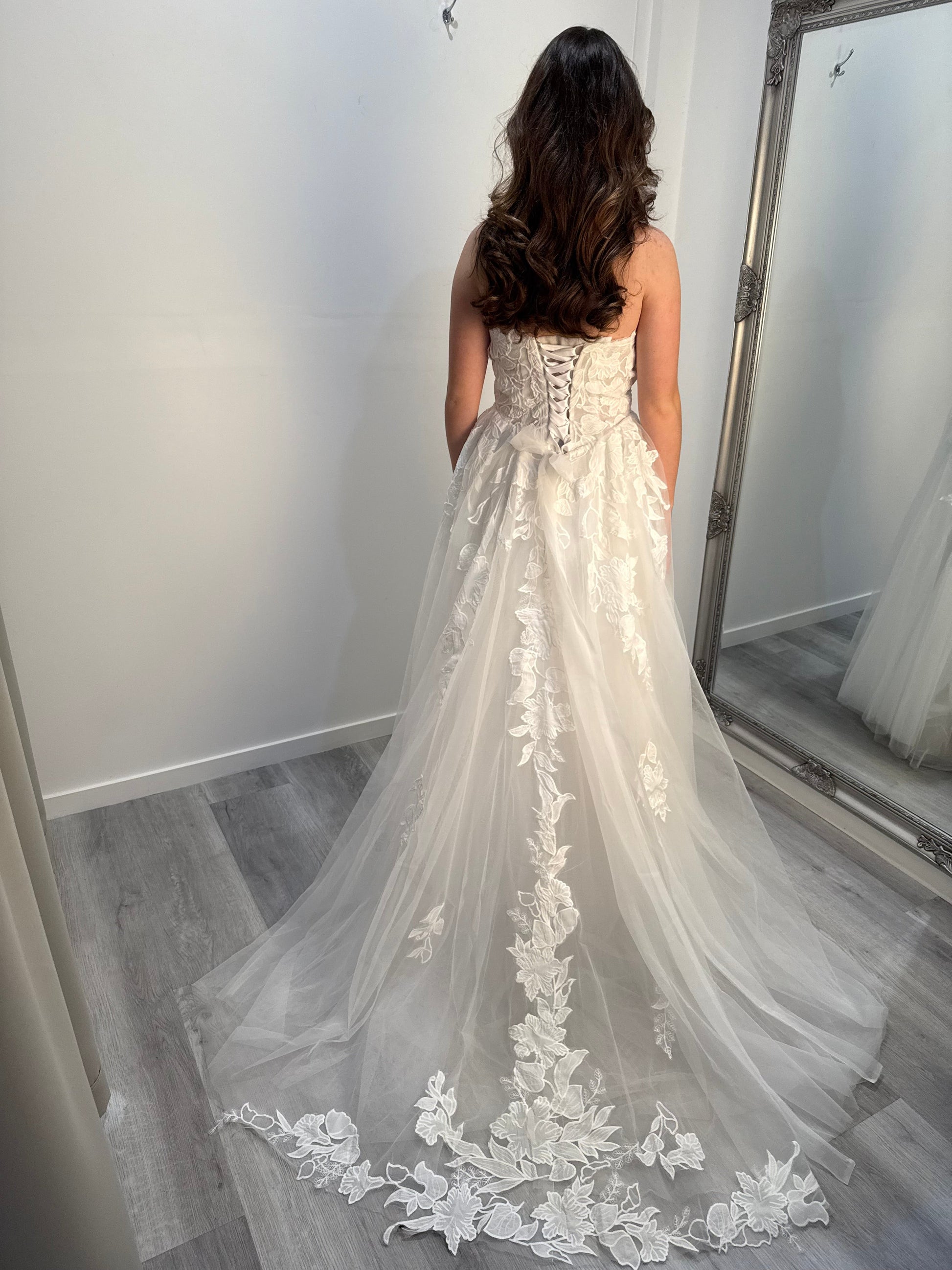 Woman wearing a ivory wedding dress with floral details in a room.