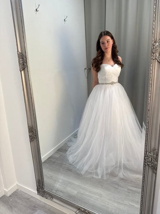 Person wearing a white dress standing in front of a large mirror.