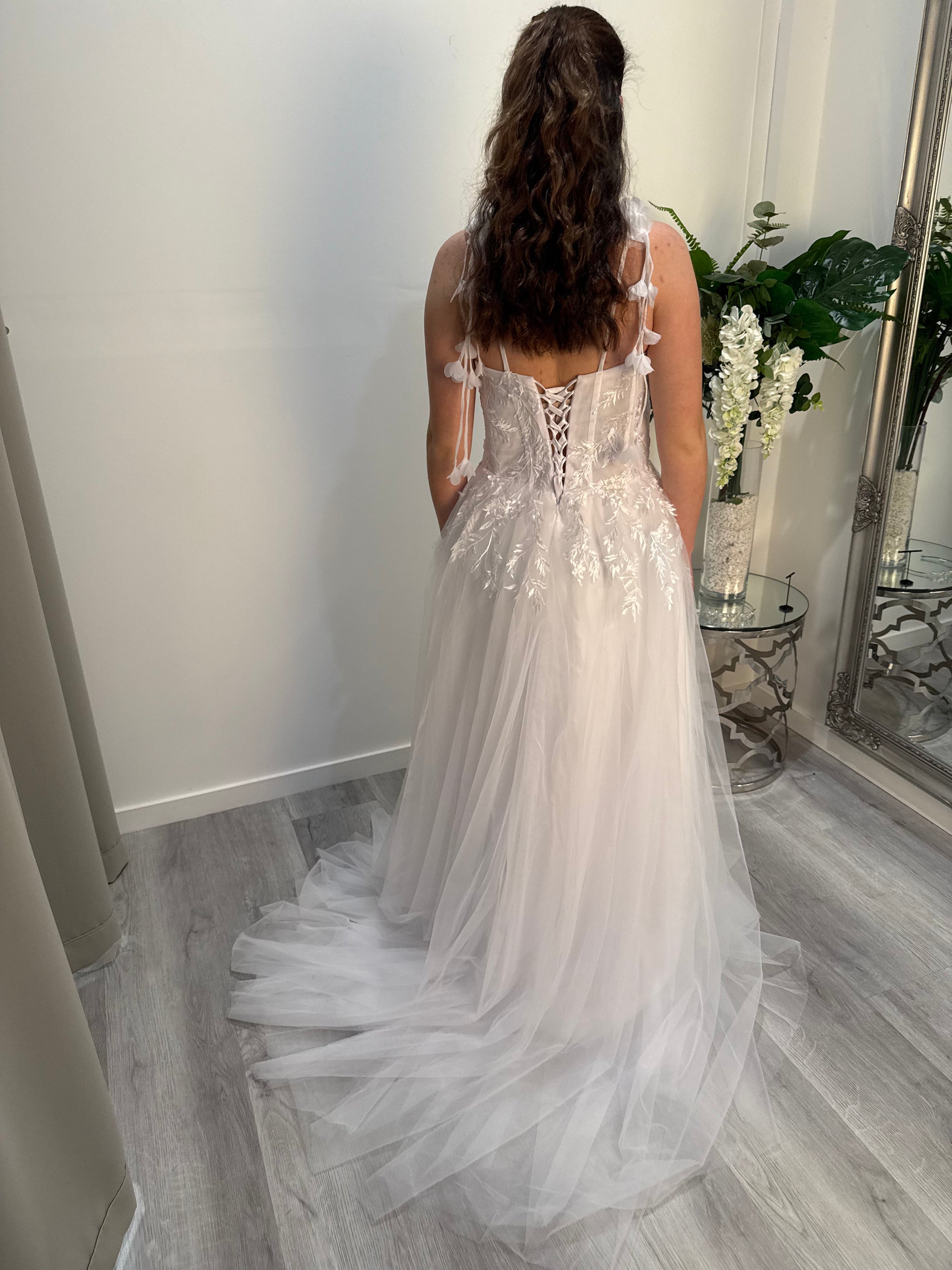 Woman in a white deb dress standing in a room with a mirror and flowers.
