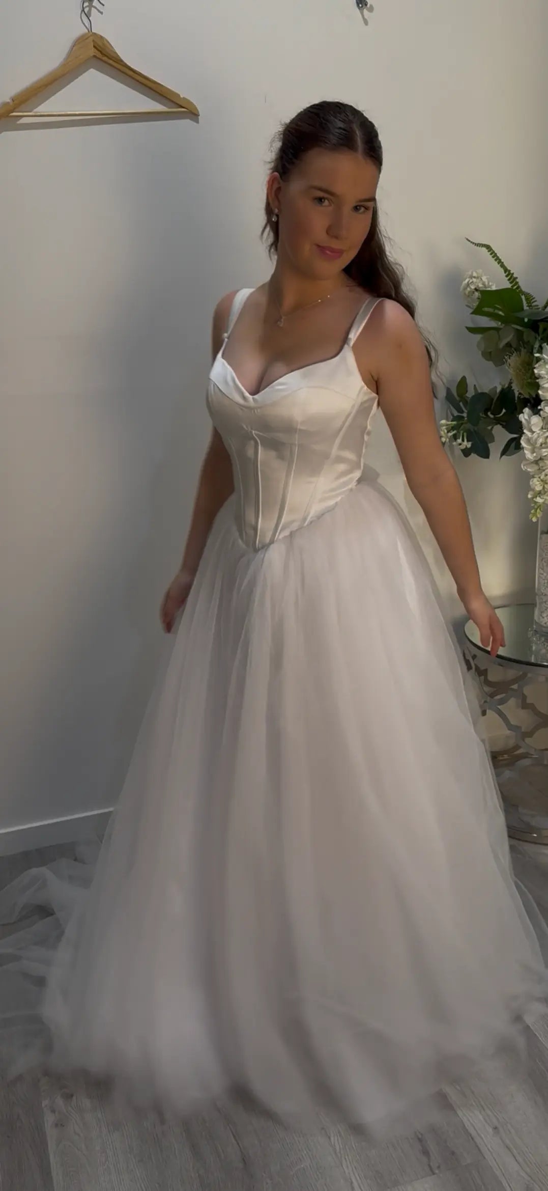 Woman standing in front of the camera, smiling and showcasing a bit of the front and side of the dress