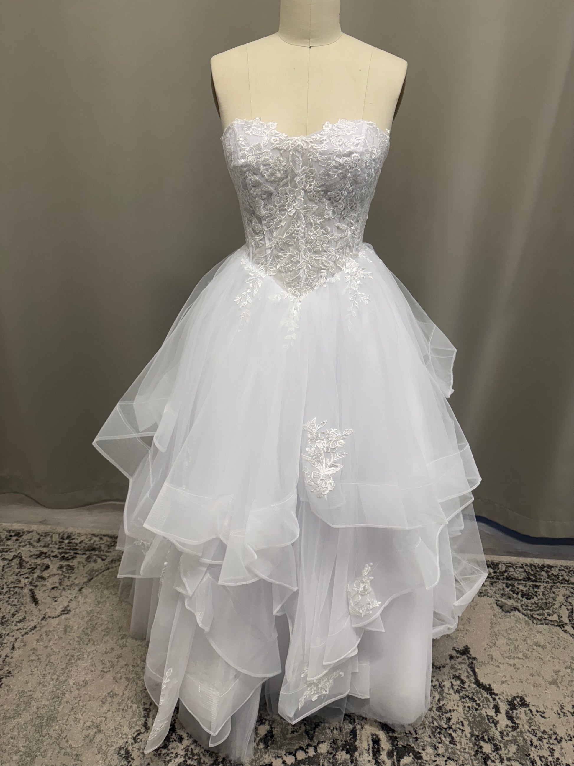 Kasey V1 white lace appliqué debutante dress, front view on mannequin with floral lace corset and full ruffle skirt