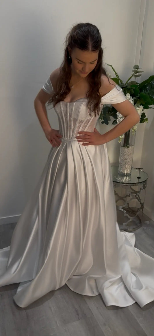 Woman wearing a white off-shoulder dress, standing to the side.
