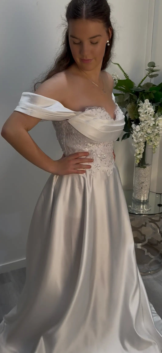 Woman wearing a white off-shoulder gown with lace details in an indoor setting.