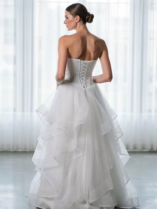 Woman wearing a strapless white deb dress with ruffled layers in a bright room.