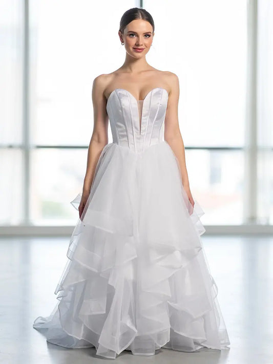 Woman wearing a white strapless deb dress with a layered skirt in front of large windows.