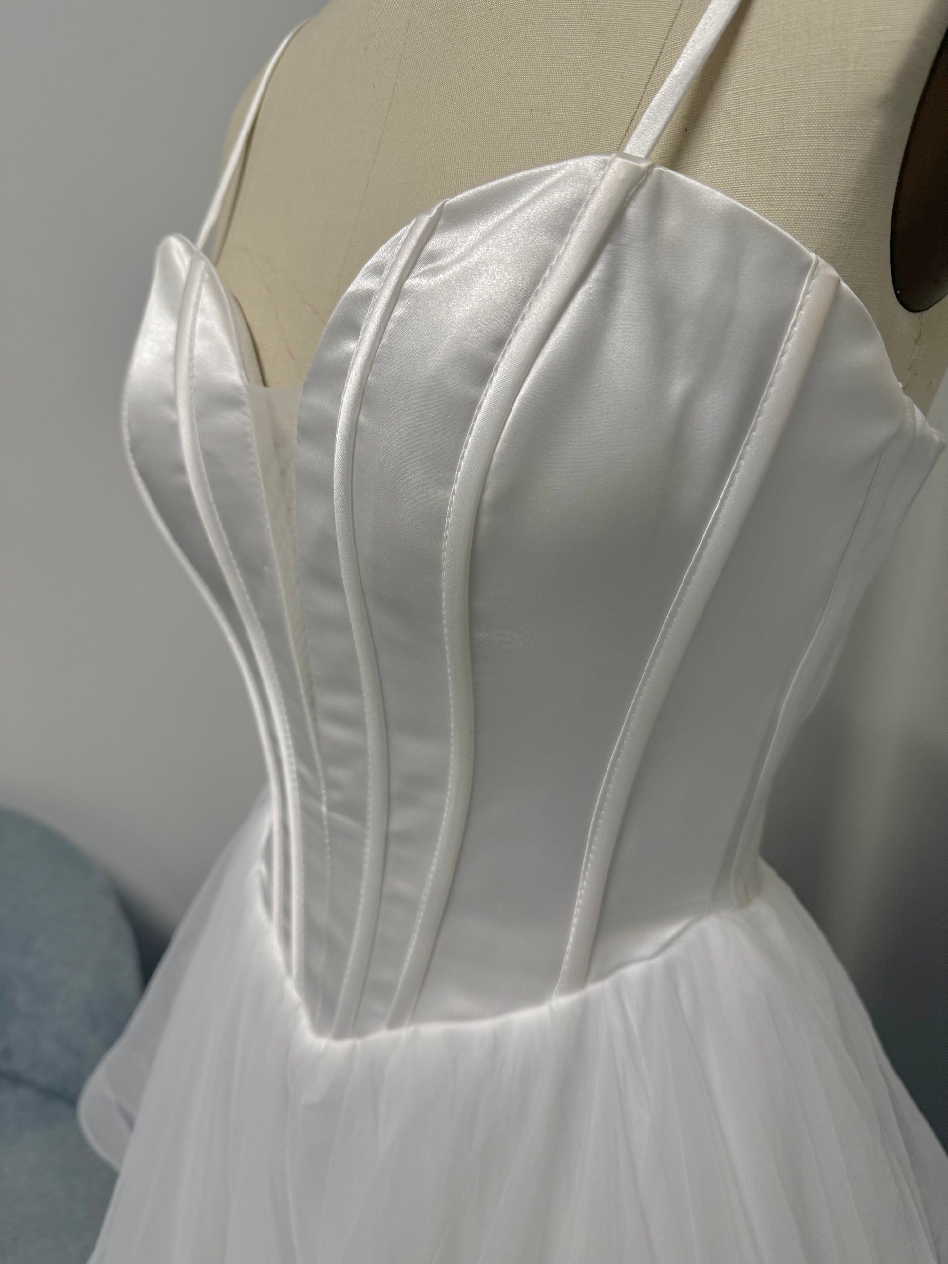 Close-up of white strapless satin corset bodice with structured boning and pleated detailing on a debutante dress.