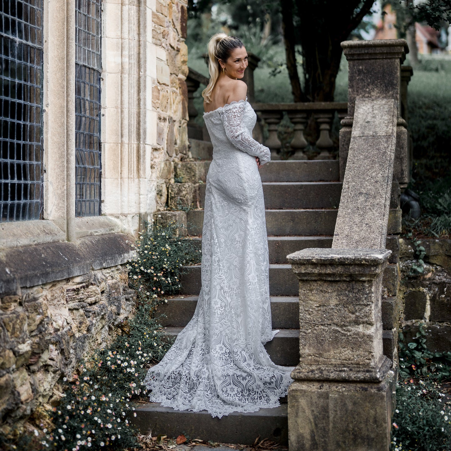 Stunning bride in the Celaya wedding dress featuring off-the-shoulder sleeves, scalloped trim, and a gracefully trailing chapel train.