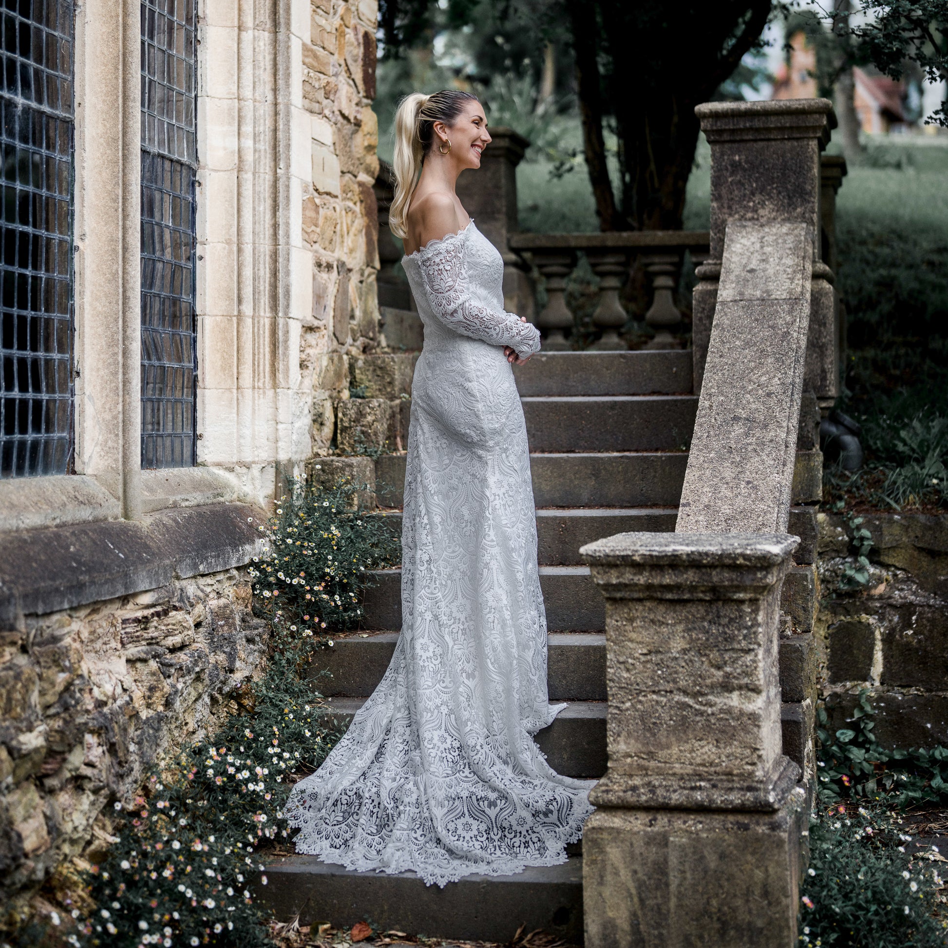 Stunning bride in the Celaya wedding dress featuring off-the-shoulder sleeves, scalloped trim, and a gracefully trailing chapel train.