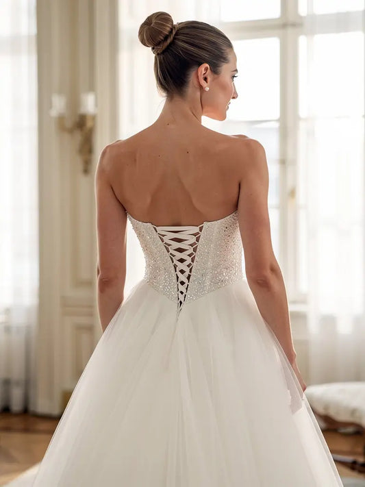 Woman wearing a white deb dress with an open back in a softly lit room.