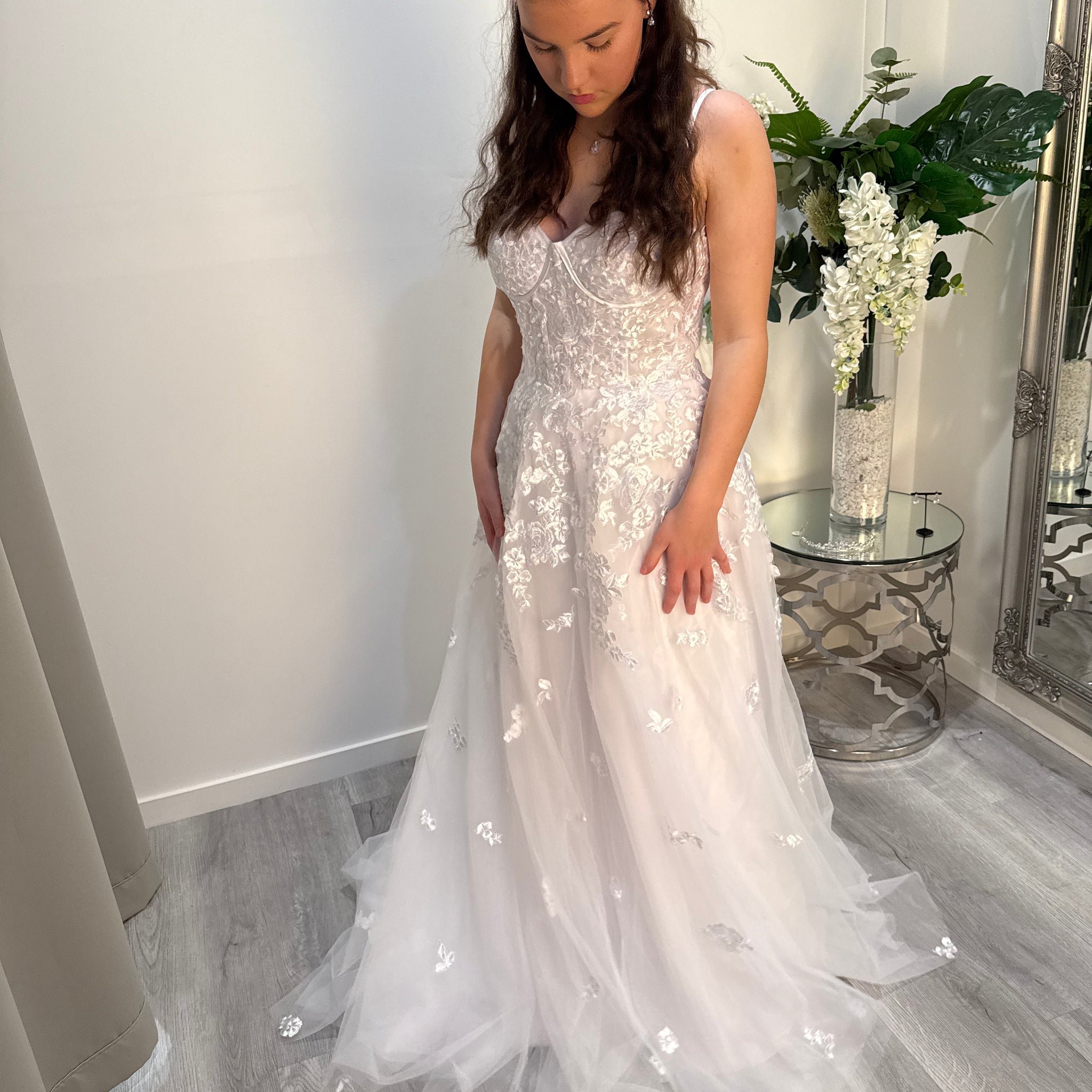 Woman in a white debutante dress standing in a room with a mirror and plants.