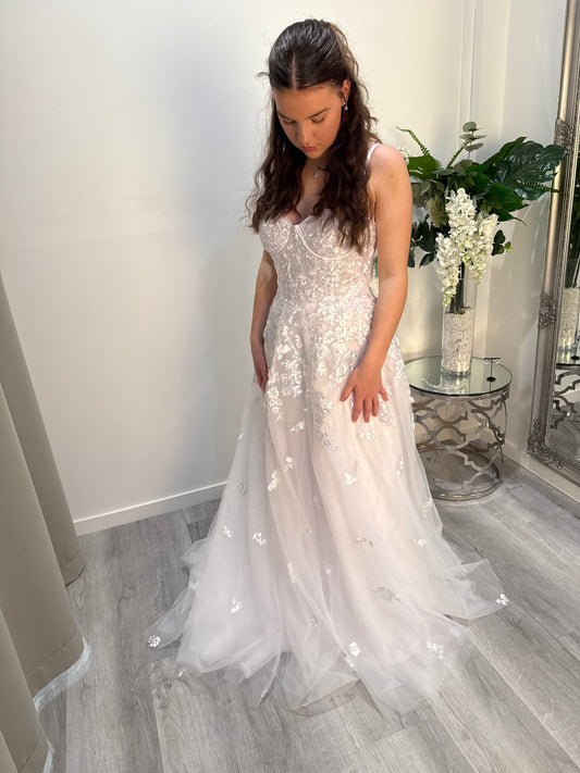 Woman in a white debutante dress standing in a room with a mirror and plants.
