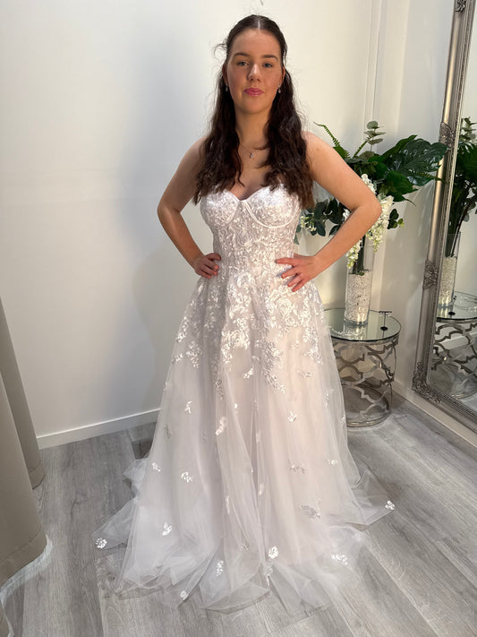 Woman in a white lace deb dress standing in a room with a mirror and plants.
