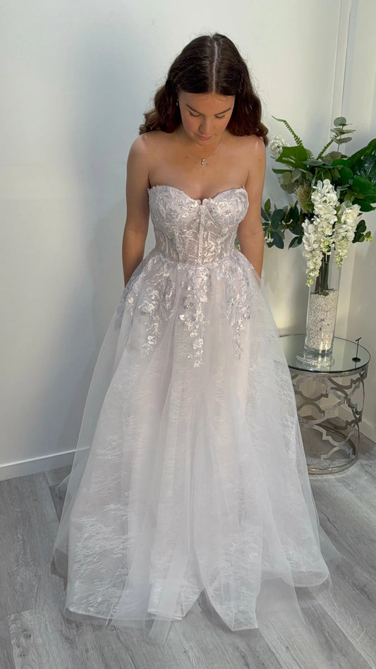 Woman wearing a strapless, floor-length wedding dress with floral embellishments, looking down