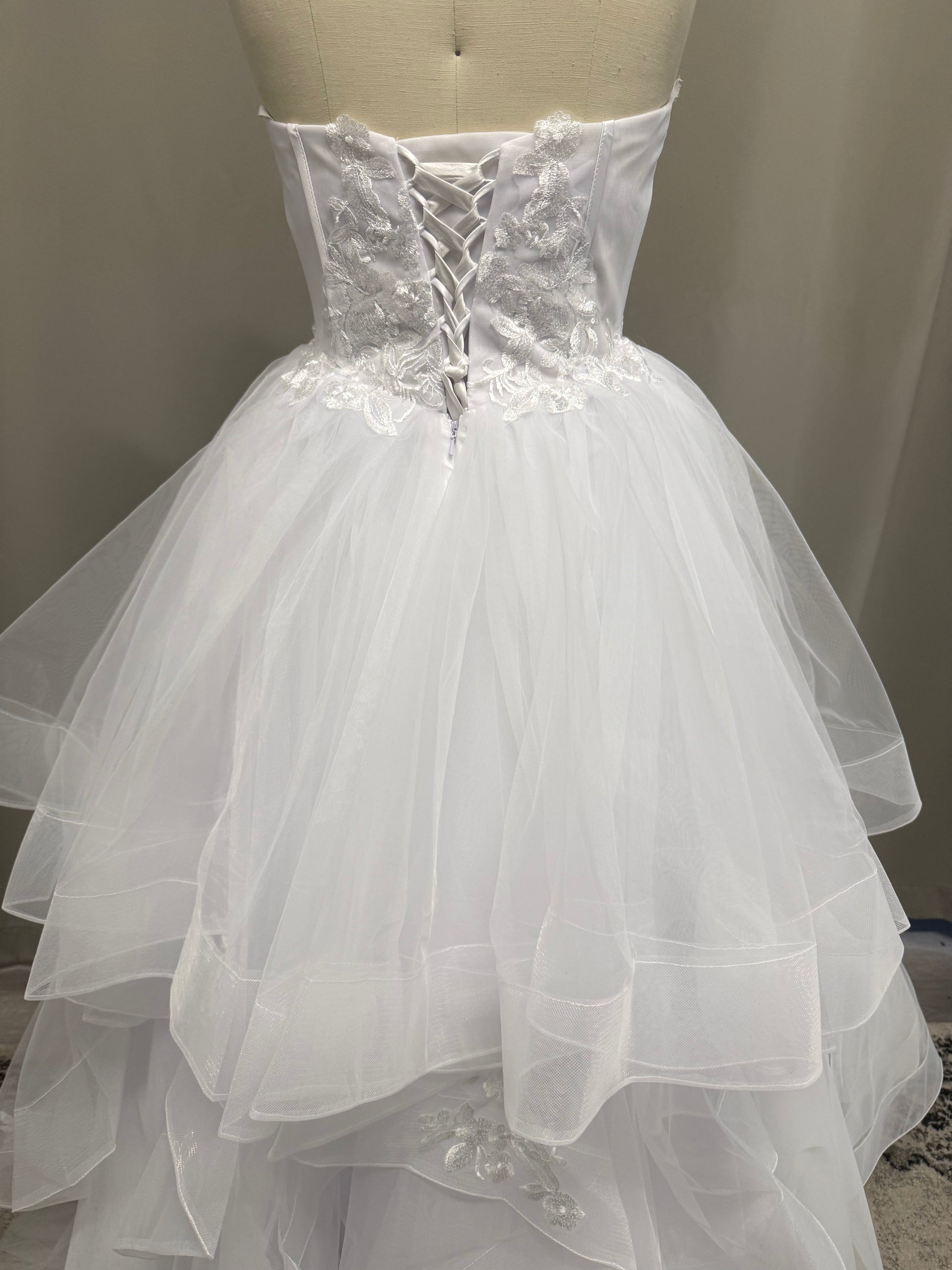 Skye V1 floral lace debutante dress back view showing lace-up corset, floral lace appliqué and full white ruffle skirt