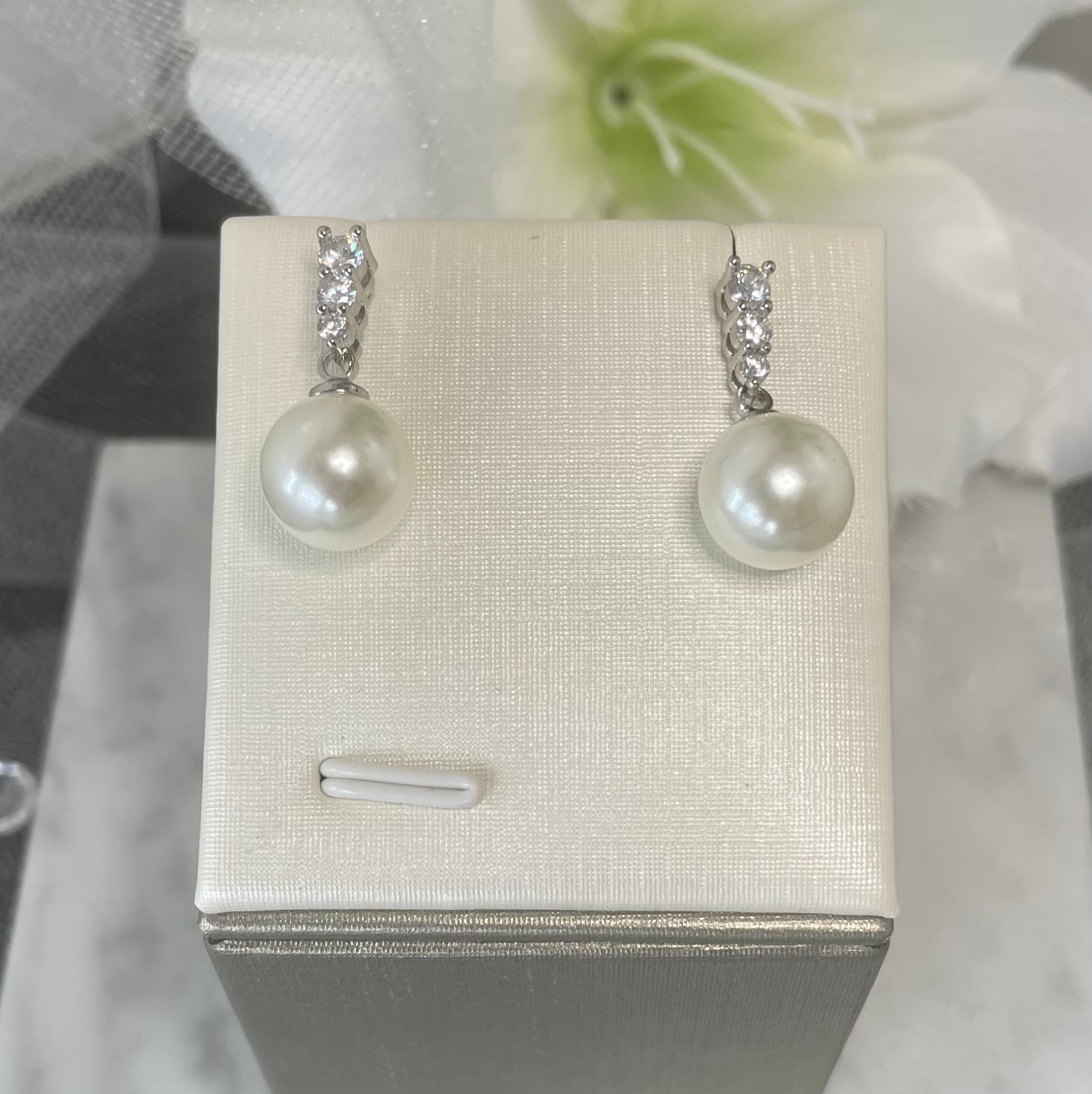 Close-up view of Everly Crystal Pearl Bridal Earrings featuring three varying-sized round crystals and a dangling pearl, perfect for elegant wedding day accessories.