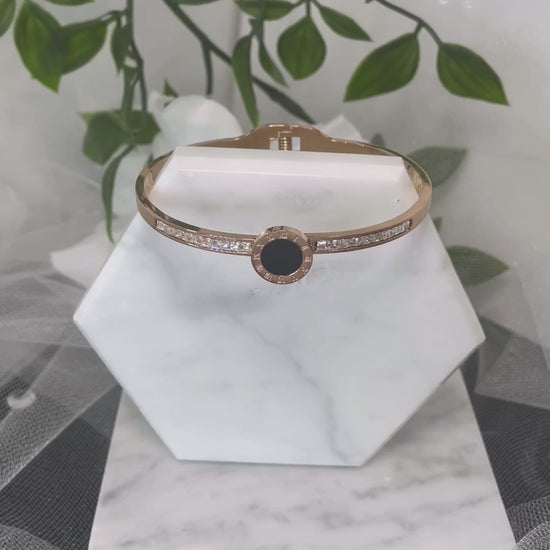 18k Rose Gold Plated CZ Bracelet featuring Roman Numerals inscribed on a black center motif, elegantly displayed on a velvet pillow.