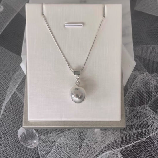 Introducing the Merleah Silver Necklace, a round silver pendant necklace with intricate design details. The pendant is complemented by a round ball. Suitable for casual and formal attire.