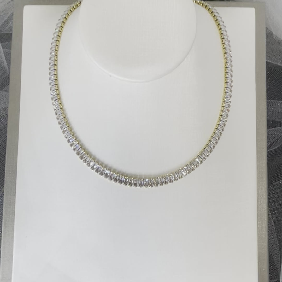 "Breanna" necklace: A gold necklace with a rectangular arrangement of Diamanté stones, shimmering and sparkling. The necklace measures 36 cm with a 3 cm extension, totaling 39 cm in length. Its elegant design rests gracefully on the collarbone, enhancing the neckline. The opulent beauty of "Breanna" makes it a captivating accessory, perfect for brides or special occasions.