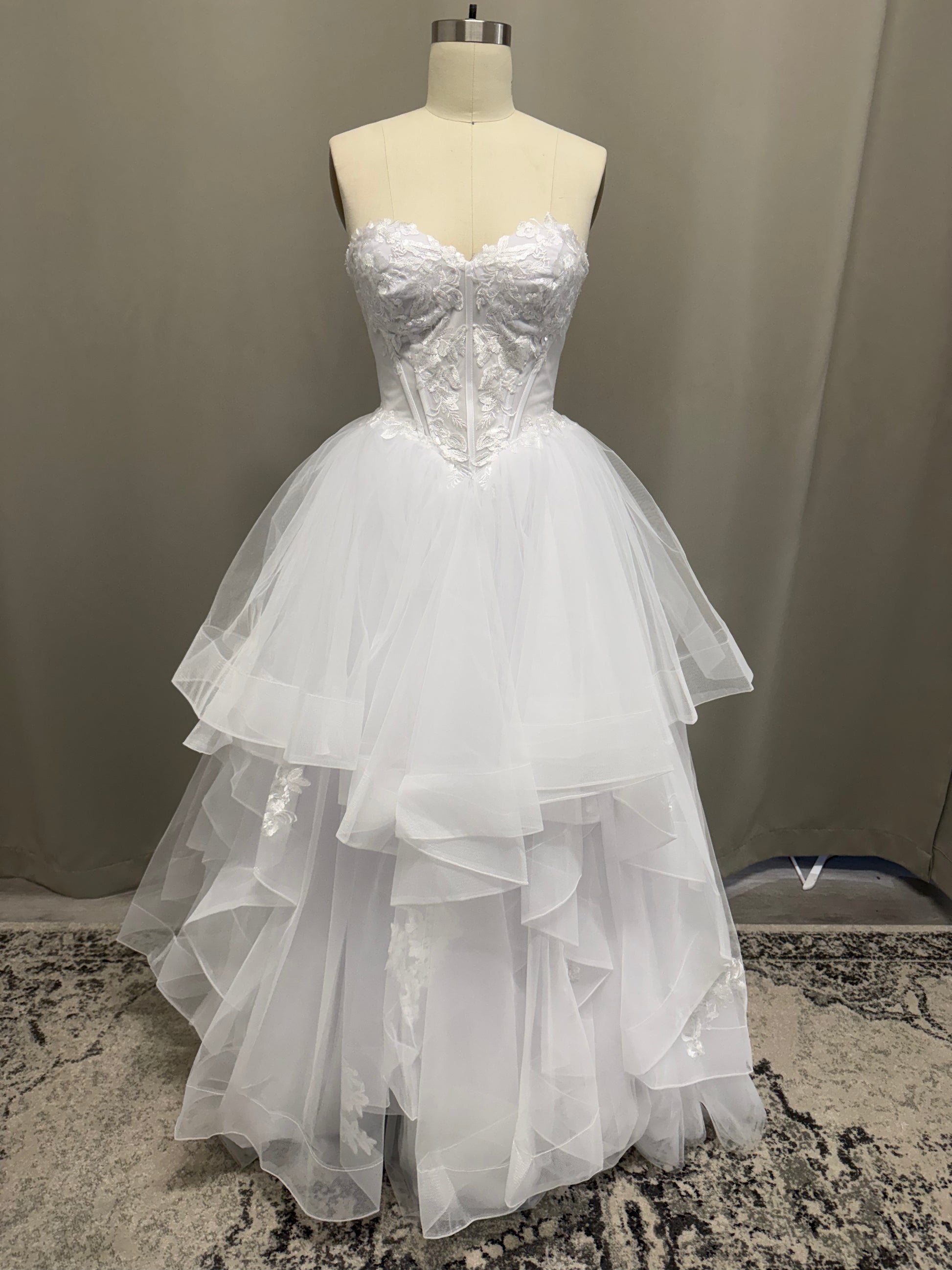 Skye V1 white floral lace debutante dress, front view on mannequin with strapless corset and full ruffle skirt